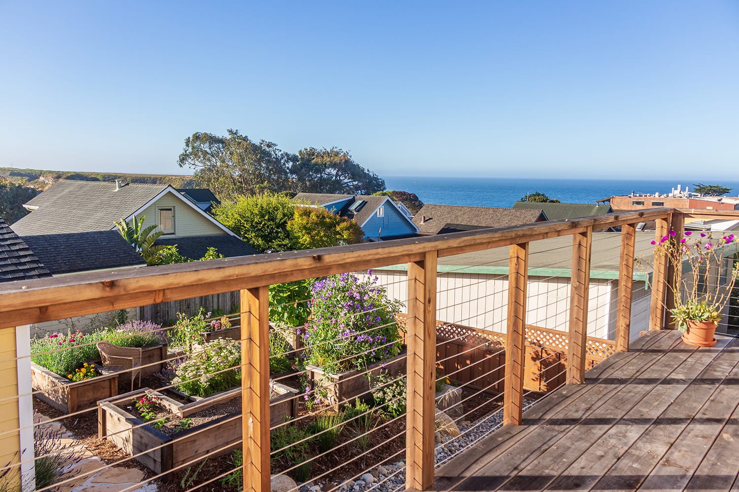 Davenport-Residence-ocean-view-from-deck-with-garden view of Pacific Ocean from deck above residential landscape featuring raised garden beds with flowers and vegetables by California designer Braid.Work Landscape Architecture